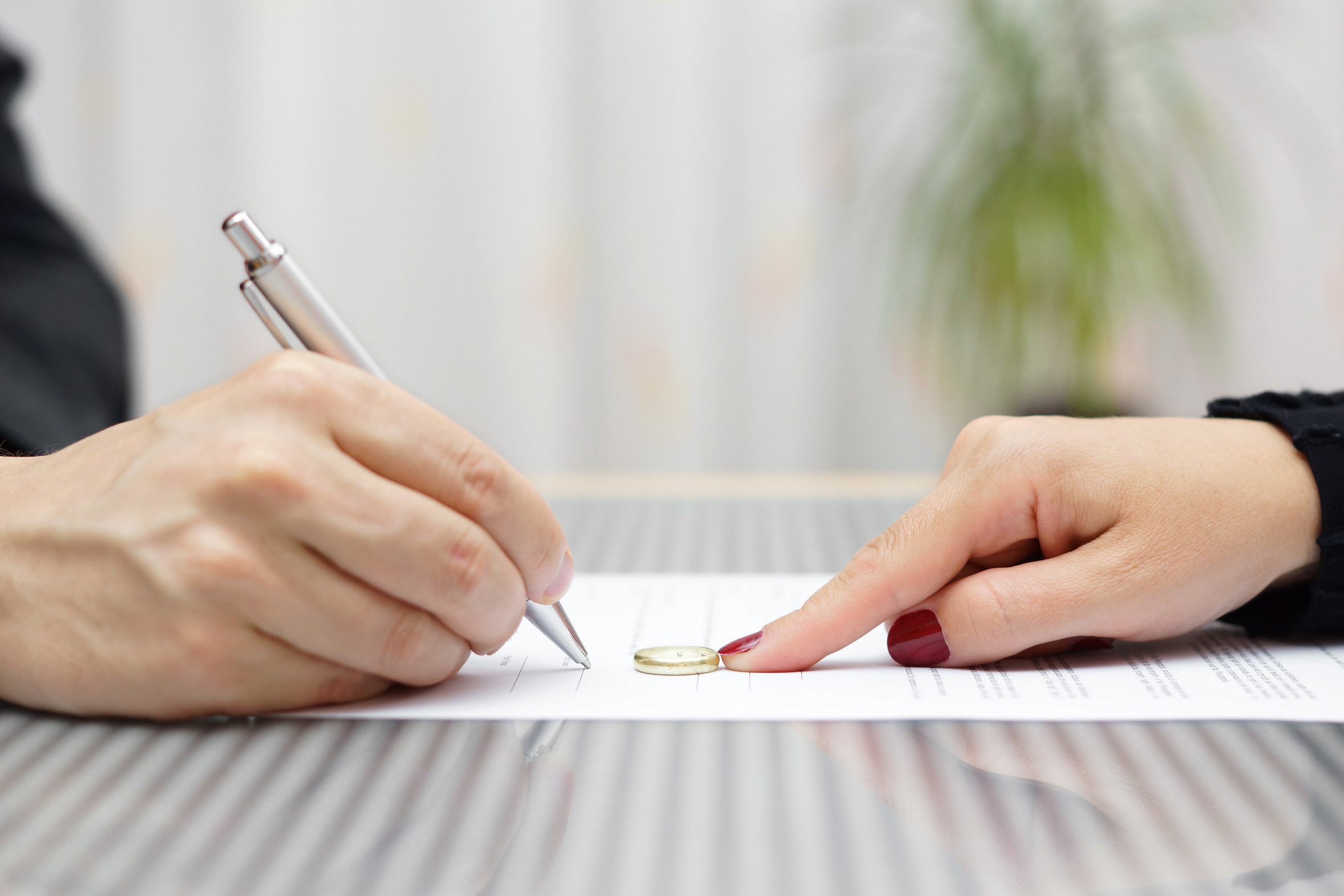 woman's hand pointing at a line to sign on paper to man with pen in hand; Divorce and Business Impact concept image