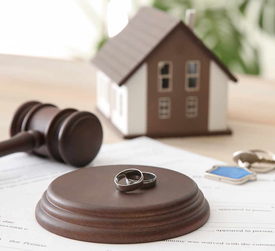 small house model, wedding rings and gavel on desk