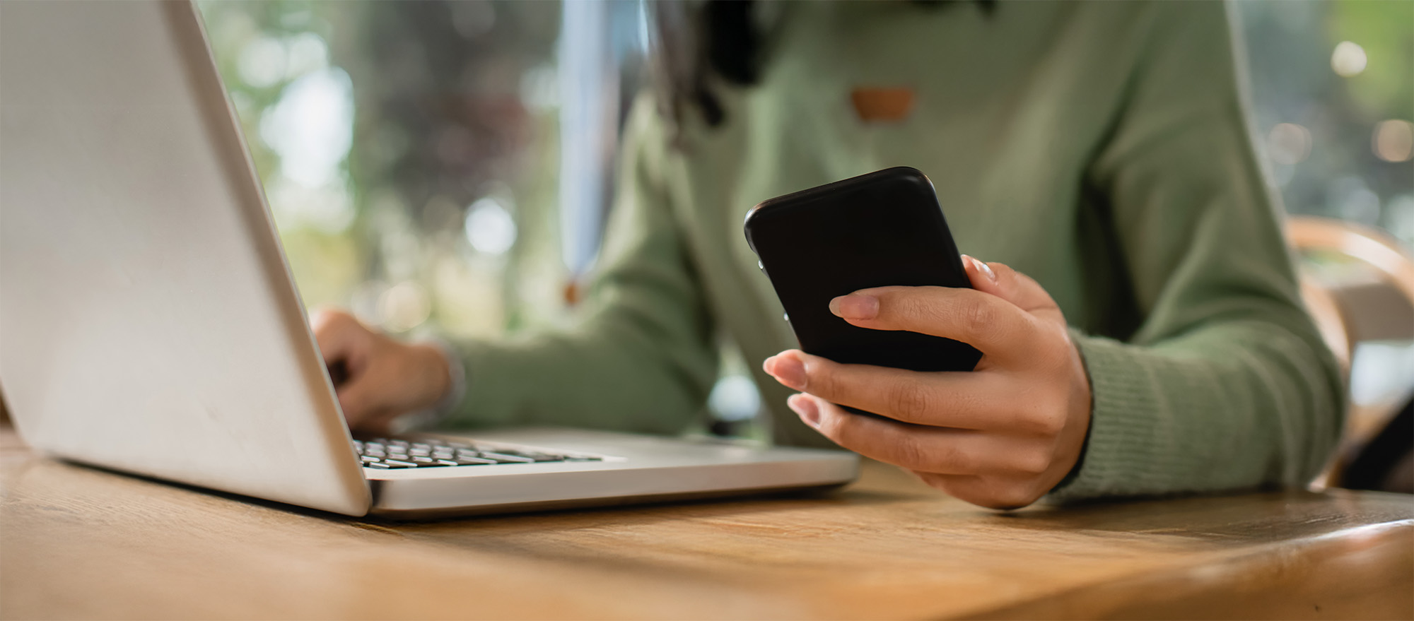 partial view of african american woman holding phone near laptop on table